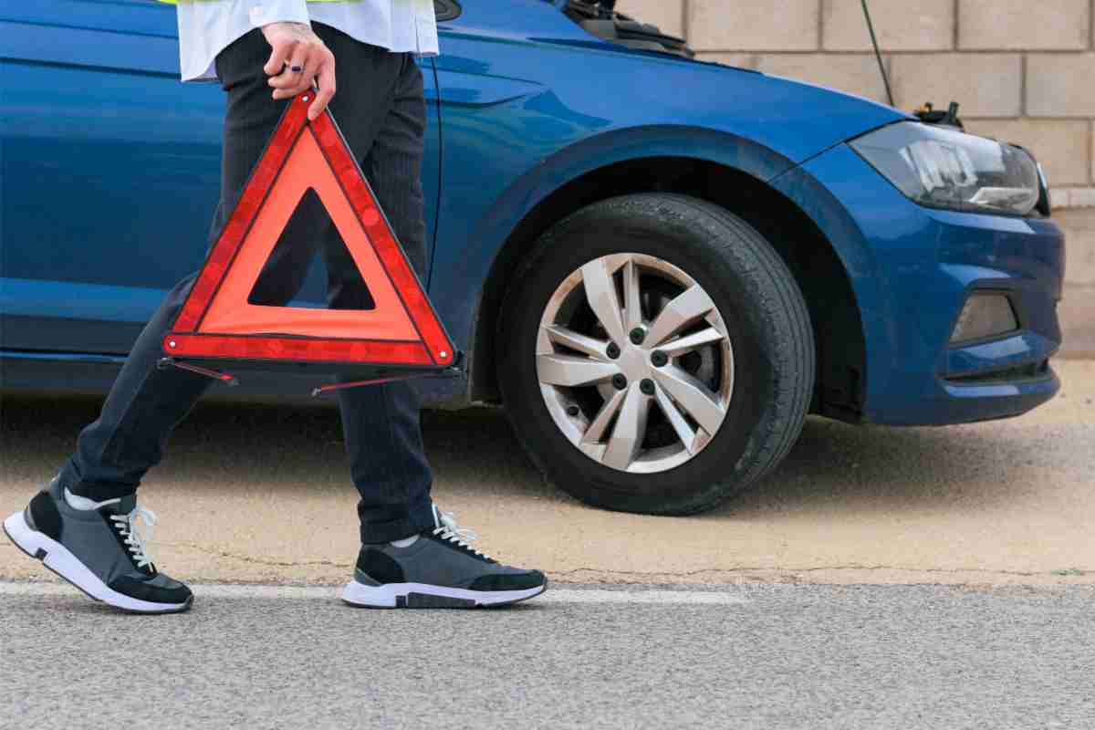 Uomo che prende il triangolo d'emergenza da posizionare davanti all'auto incidentata