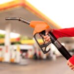 persona che tiene una pompa della benzina e sullo sfondo un distributore