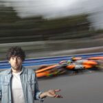 una McLaren di Formula 1 sfocata e a sinistra un ragazzo incredulo