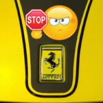 Il cofano di una Ferrari gialla con il logo e il nome e sopra un emoticon con il cartello Stop